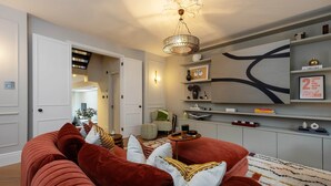 Ein Wohnzimmer mit einem roten Sofa, einer Chandelüster und einer Wand mit Regalen.
