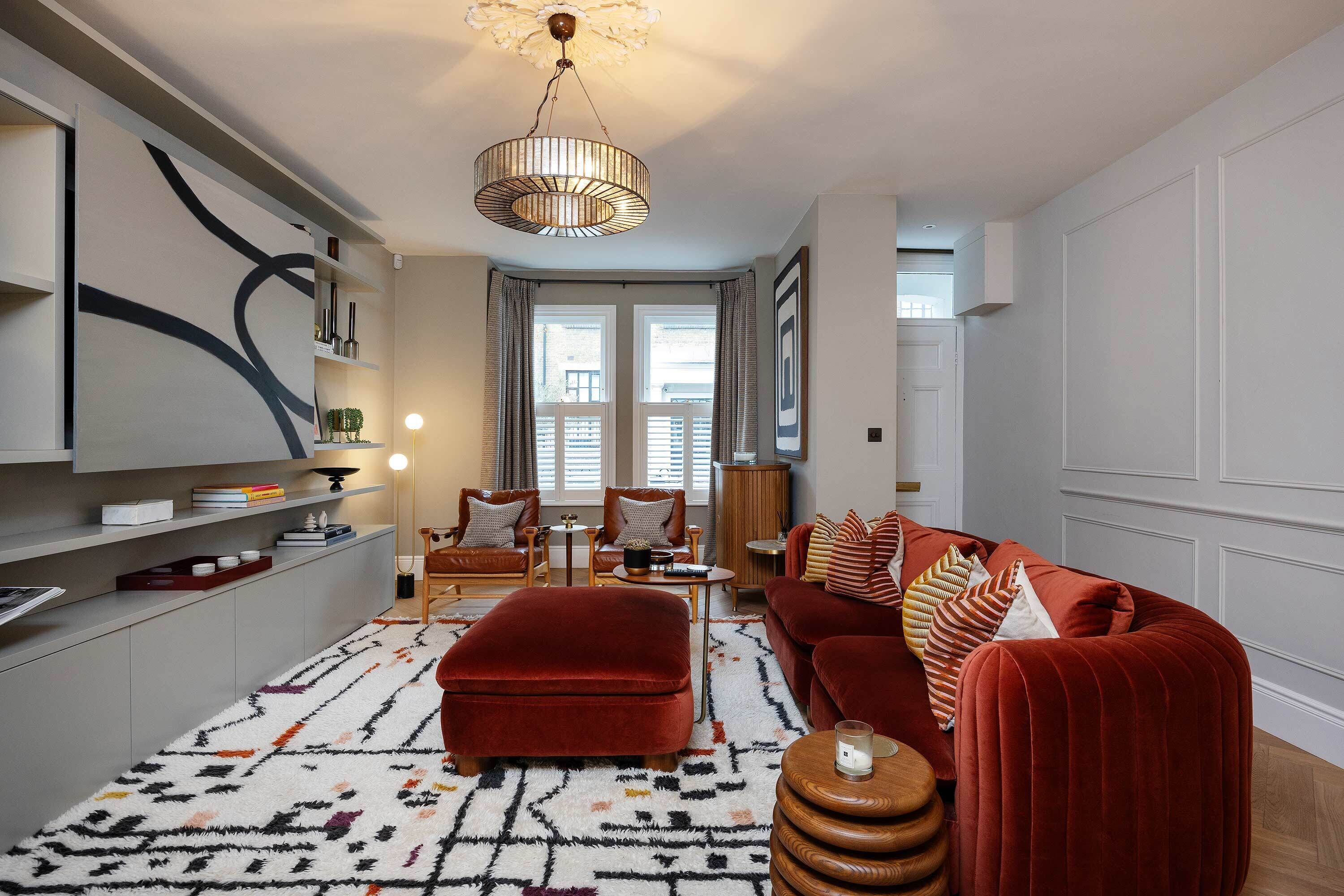 A modern living room with a red velvet sofa, a patterned rug, and a pendant light.