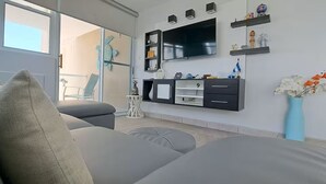 Ein modernes Wohnzimmer mit einem grauen Sofa, einem an der Wand befestigten Flachbildfernseher und einem kleinen Couchtisch mit Dekoration.