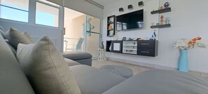 Ein modernes Wohnzimmer mit einem grauen Sofa, einem an der Wand befestigten Flachbildfernseher und einem kleinen Couchtisch mit Dekoration.