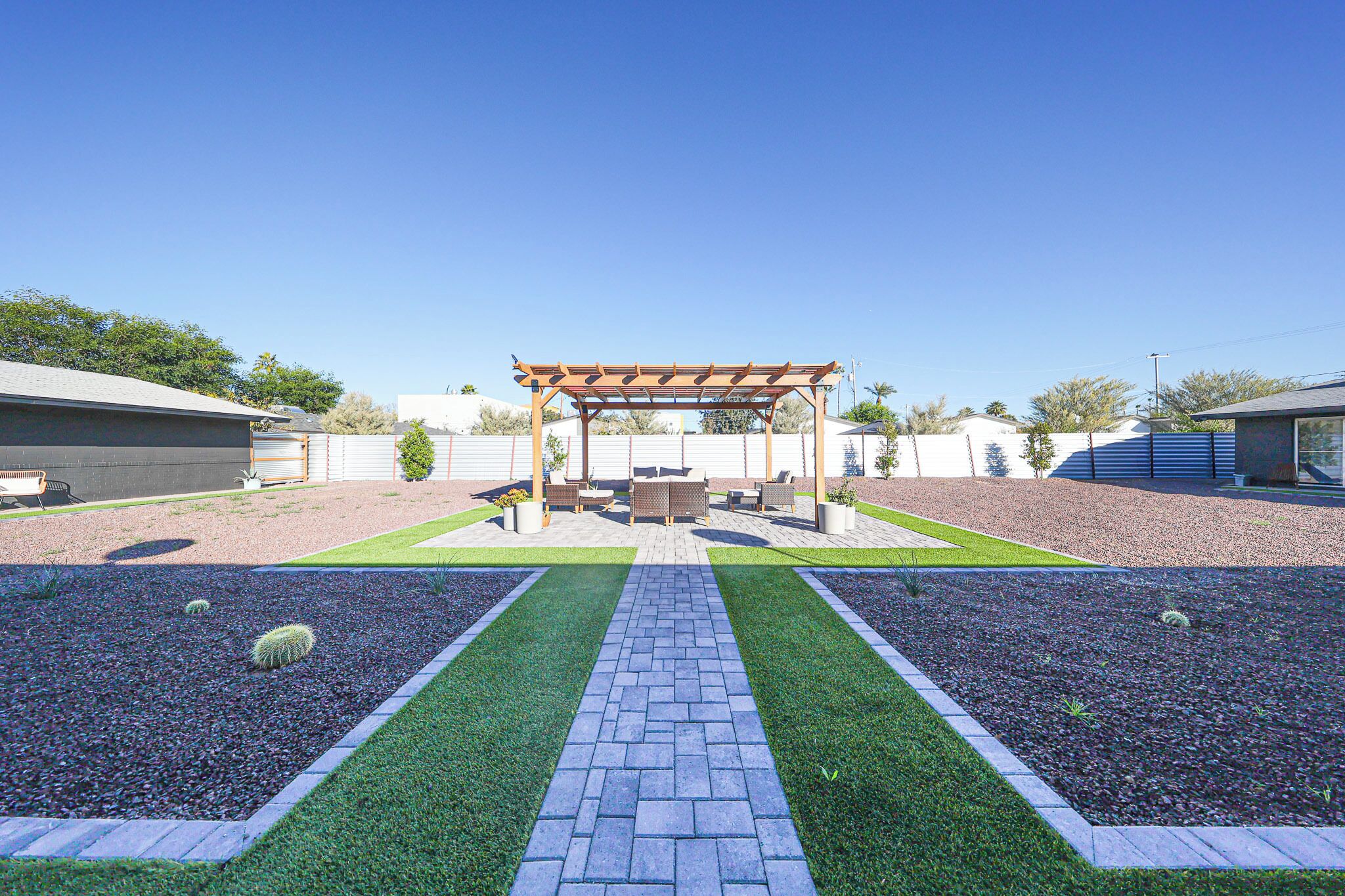 Eine Terrasse mit einer Pergola, Sitzgelegenheiten und einem gepflasterten Weg.