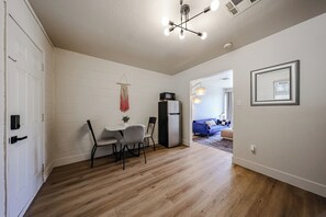 Ein Zimmer mit Esstisch, Stühlen, einem Kühlschrank, einer hängenden Pflanze und einem blauen Sofa im Hintergrund.