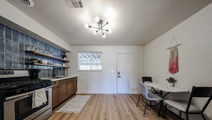 Une cuisine équipée d’une cuisinière, d’un four et d’étagères, un coin repas avec une table et des chaises, et une porte blanche.