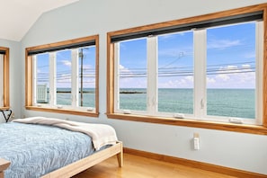 A bedroom with a bed, two windows with wooden frames, and a view of the sea. - Wells Home with Ocean & Marsh Views + Beach Access (Wells)