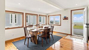 Un coin repas avec une table dressée pour quatre personnes, de grandes fenêtres équipées de volets et une vue sur l’océan.