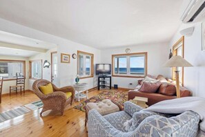 A spacious living area with a television, comfortable seating, and large windows offering a view of the sea.