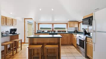 A modern kitchen with wooden cabinets, a large island with bar stools, a built-in oven, and a view of the outdoors.