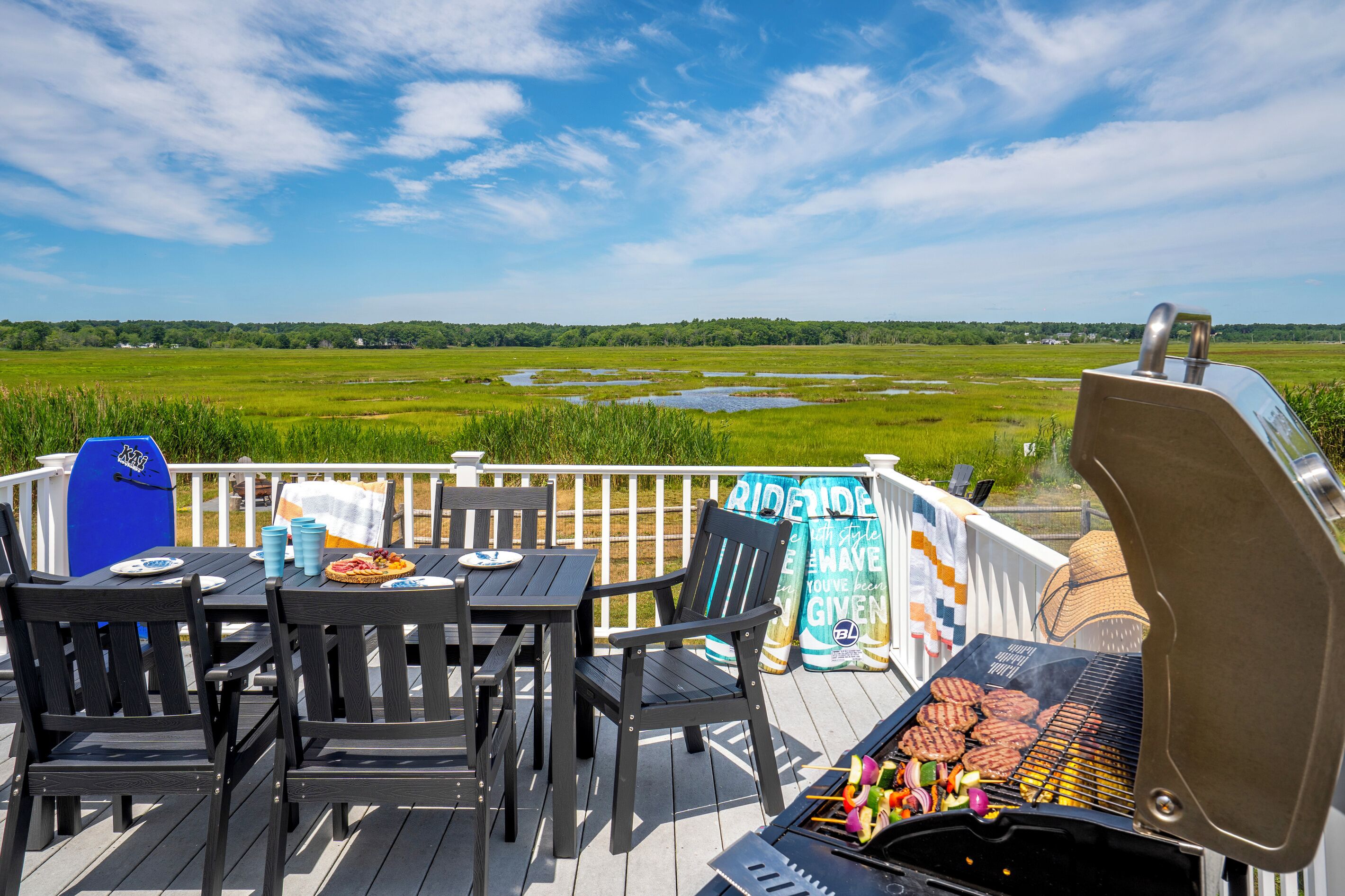An outdoor deck with a grill, seating, and a view of a wetland.
