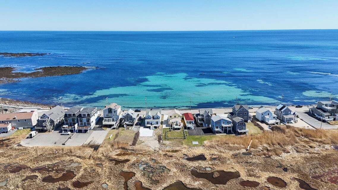 A coastal residential area with houses, a clear view of the ocean, and a sandy beach.