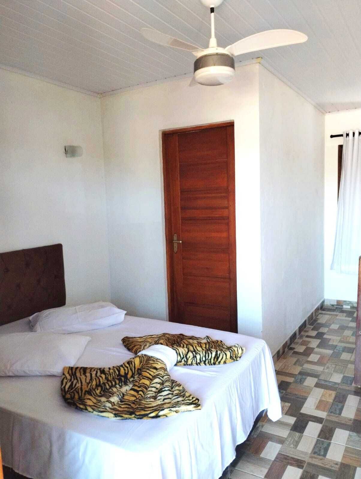 Un lit simple avec une tête de lit en bois, un ventilateur de plafond et une porte en bois.