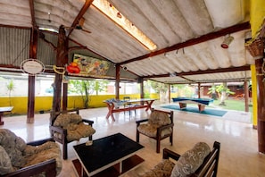 A covered outdoor seating area with tables, chairs, and a pool table.
