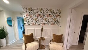 Een hal met twee fauteuils, een klein bijzettafeltje en een wanddecoratie met bloemenprint.