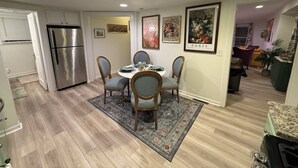 Een eethoek met een tafel gedekt voor vier personen, omringd door stoelen, een vloerkleed en een koelkast.