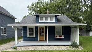 Een gelijkvloers huis met een veranda, een voordeur en een kleine tuin.