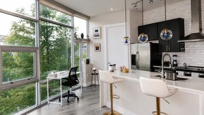 A modern kitchen with large windows, a central island, and a dining area with chairs.