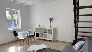 Un comedor con una mesa y sillas, un aparador blanco con objetos decorativos, un sofá gris con cojines y una escalera.