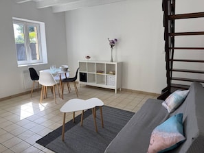 Ein Essbereich mit Tisch und Stühlen, ein weißer Konsolentisch mit Dekoration, ein graues Sofa mit Kissen und eine Treppe.
