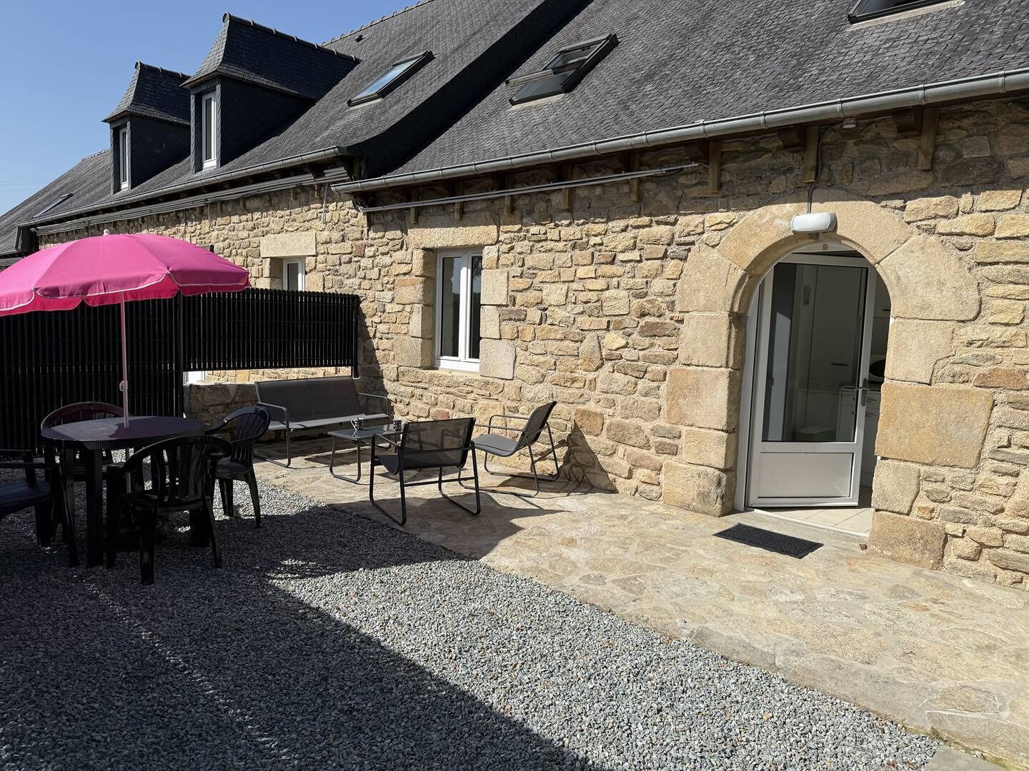 A stone building with a sloped roof, a patio with outdoor seating, and a door with a glass panel.