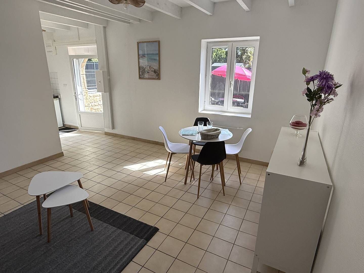 A dining area with a round table, white chairs, a small rug, and a vase with flowers.