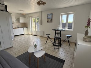 Eine moderne Küche mit weißen Schränken, ein Essbereich mit einem runden Tisch und Hockern sowie ein großes Fenster mit Aussicht.