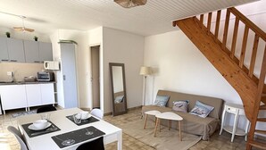 A modern kitchen with white cabinets, a dining table with chairs, a sofa with cushions, a mirror, and a wooden staircase. - NEW LISTING, Domaine de KER-PAULT, between St Cast and Matignon, 2-bedroom apartment 5 minutes... (MATIGNON)