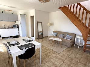 Eine moderne Küche mit weißen Schränken, einem Esstisch mit Stühlen, einer Couch mit Kissen, einem Spiegel und einer Holztreppe.
