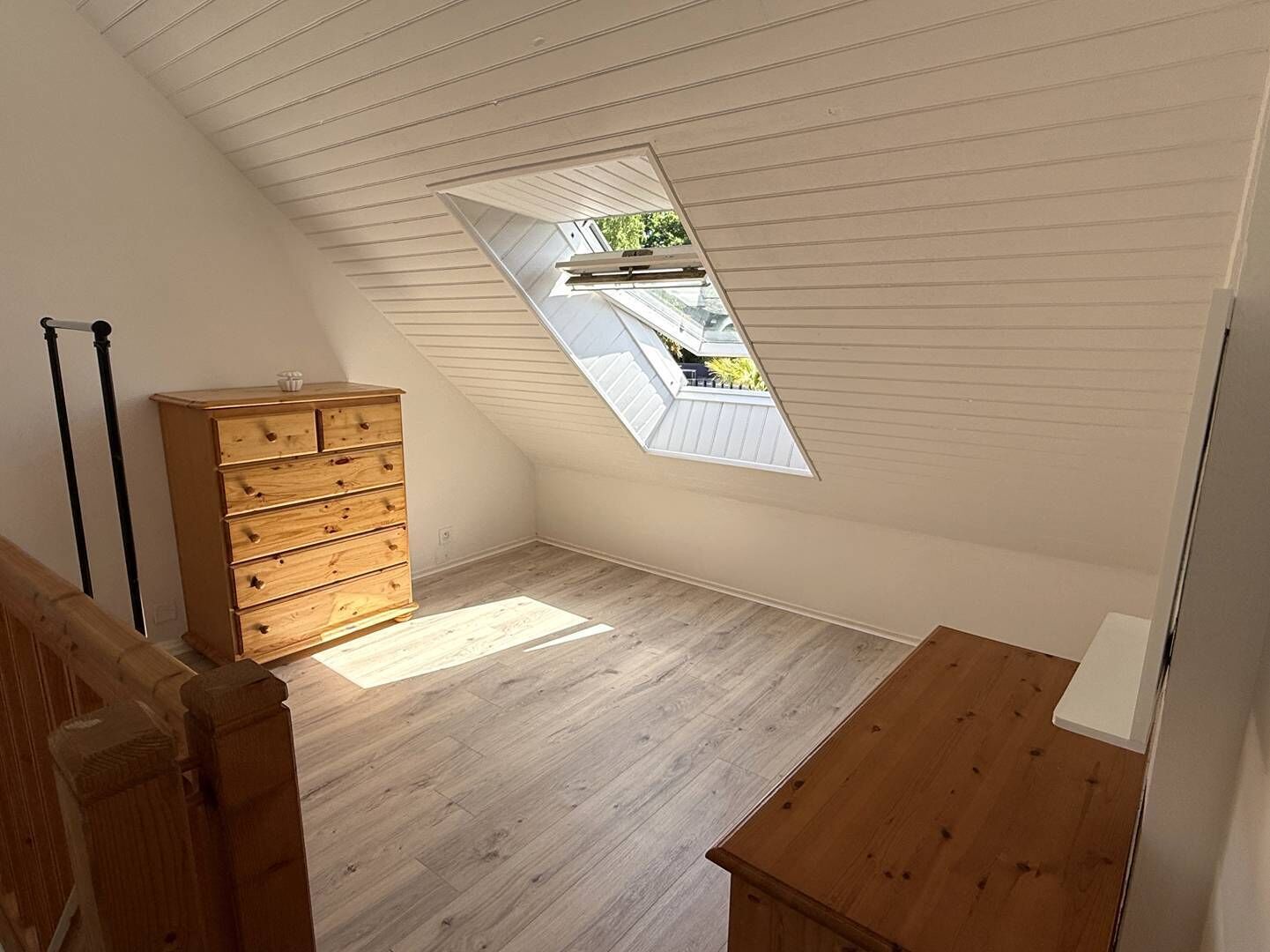 A room with a sloped ceiling, a wooden dresser, a small table, and a skylight.