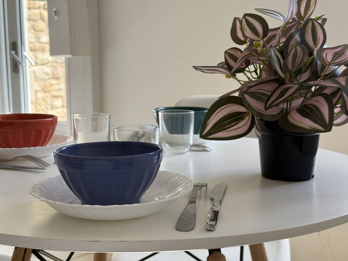 A table with a blue bowl, a knife, and a plant in a black pot.