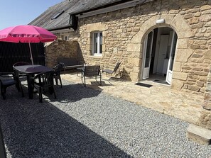 A stone building with a patio area featuring a table and chairs, a red umbrella, and a stone wall. - NEW LISTING, Domaine de KER-PAULT, between St Cast and Matignon, 2-bedroom apartment 5 minutes... (MATIGNON)