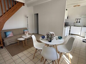 A modern kitchen with white cabinets, a dining area with a round table and four chairs, and a staircase leading to an upper level. - NEW LISTING, Domaine de KER-PAULT, between St Cast and Matignon, 2-bedroom apartment 5 minutes... (MATIGNON)