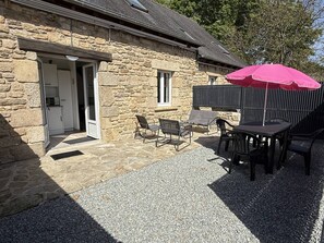 Un bâtiment en pierre doté d’un patio aménagé avec des sièges extérieurs et un grand parasol.