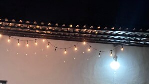 Une terrasse extérieure agrémentée de guirlandes lumineuses, une table avec des chaises et un pot de fleurs.