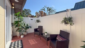 Eine Terrasse mit Korbmöbeln, Topfpflanzen und einem weißen Zaun.