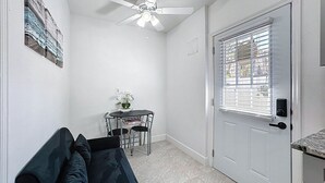 Ein kompakter Wohnraum mit Deckenventilator, einer Tür mit Fenster, einem kleinen Esstisch mit Stühlen und einer Couch.