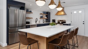Una cocina moderna con una isla central, electrodomésticos de acero inoxidable e iluminación colgante.