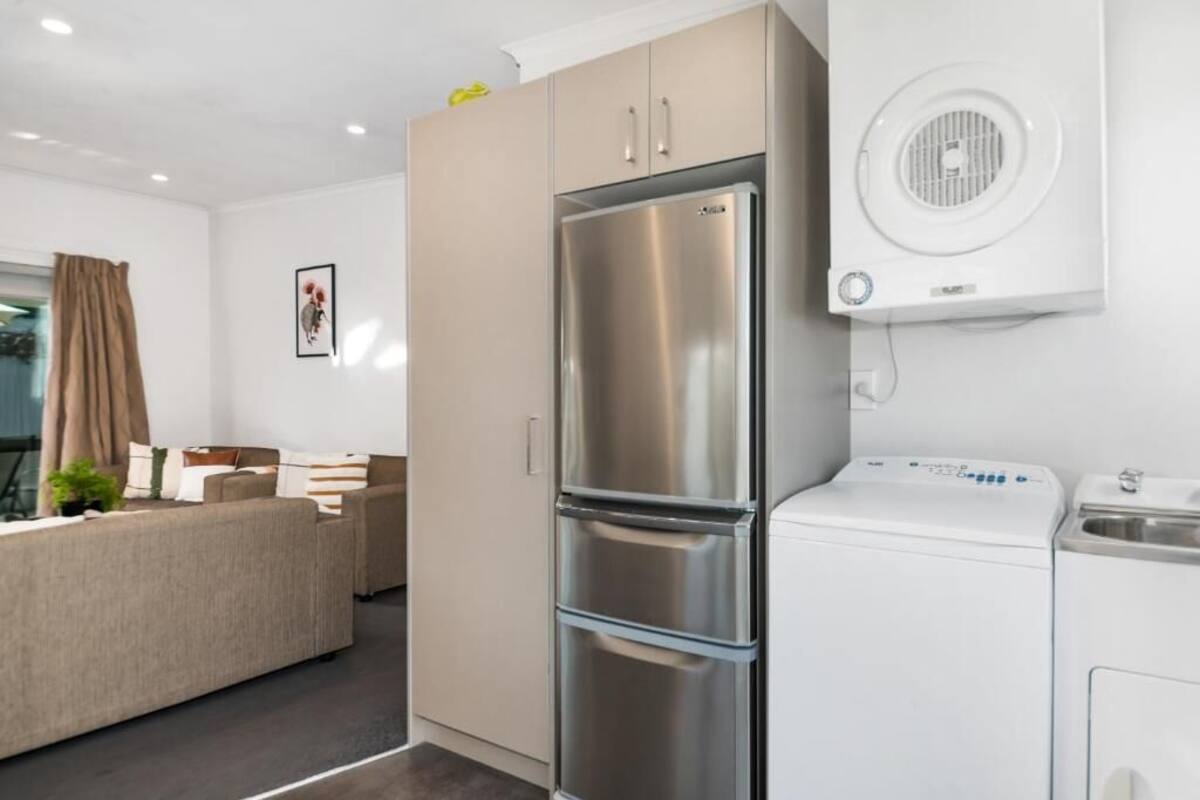 Una cocina moderna con un refrigerador de acero inoxidable, una lavadora integrada y un lavamanos pequeño.
