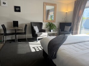 Habitación de hotel con cama, dos sillas, una mesita, escritorio, espejo y planta en maceta.
