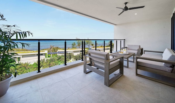 A balcony with a view of the sea, a ceiling fan, and a seating area with a table.