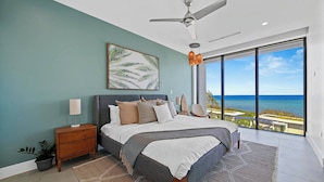 A bedroom with a bed, nightstand, and a view of the ocean.