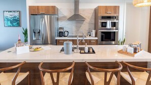 A modern kitchen with a central island, stainless steel appliances, and wooden chairs.