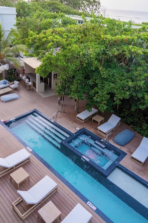 A rooftop pool with lounge chairs, a hot tub, and a view of the ocean.