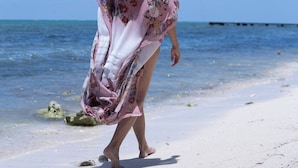 A beach scene with a person walking on the sand.