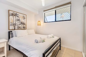 Ein Schlafzimmer mit Bett, Nachttisch, Wandbild, Fenster mit Ausblick und einer kleinen Wandleuchte.