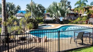 A swimming pool with a curved design, surrounded by a fence and palm trees. - Sea Air Number Two On Queen (Yeppoon)