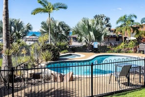 Ein Pool mit geschwungener Form, umgeben von einem Zaun und Palmen.