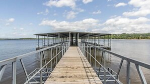 A wooden pier leading to a covered area with metal railings, overlooking a calm body of water.