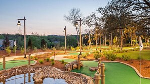 A miniature golf course with a pond, green fairways, and wooden structures.