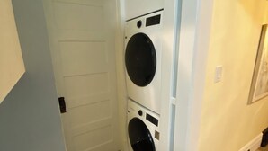 A laundry room with two stacked washing machines, a white door, and wooden flooring. - Charming home in Lethbridge with piano, beautiful neighborhood, central location (Lethbridge)