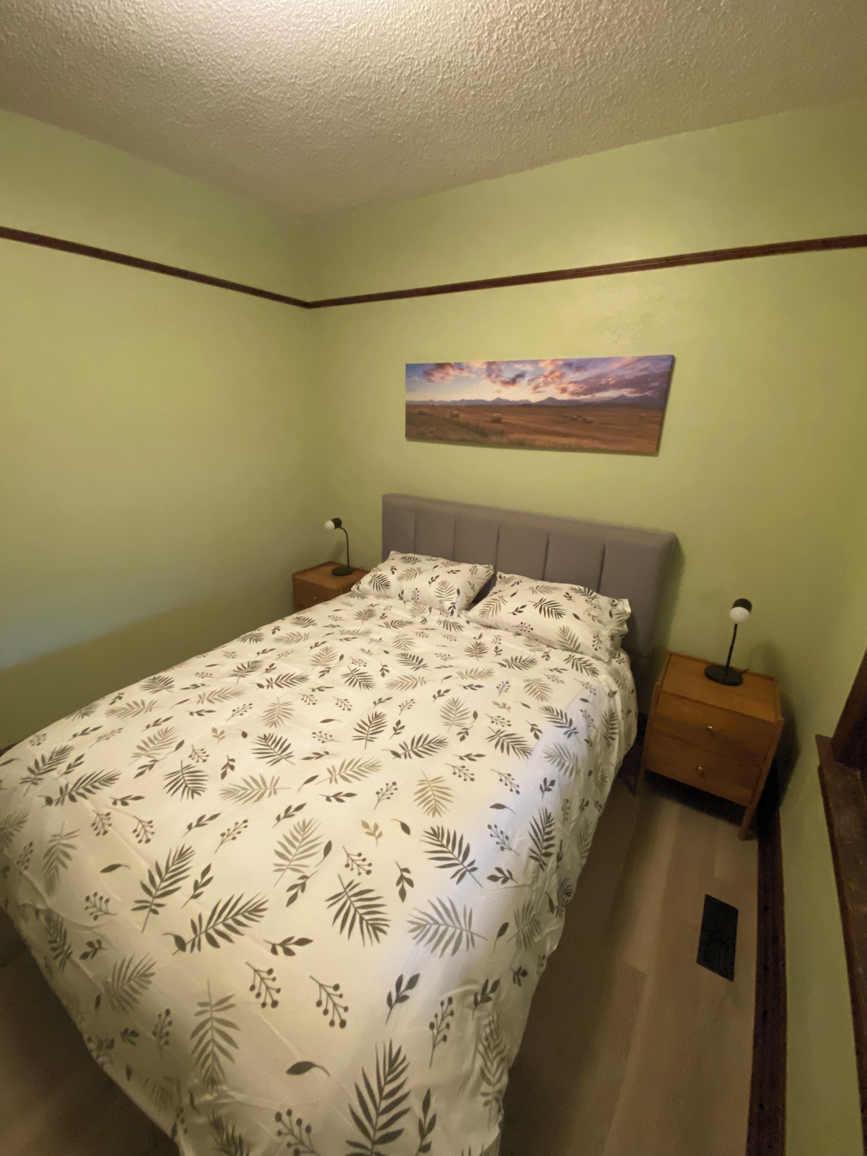 A bedroom with a bed, nightstands, a lamp, a painting, and a wooden headboard.