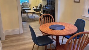 A dining area with a round wooden table, four chairs, a chandelier, and a piano in the background. - Charming home in Lethbridge with piano, beautiful neighborhood, central location (Lethbridge)